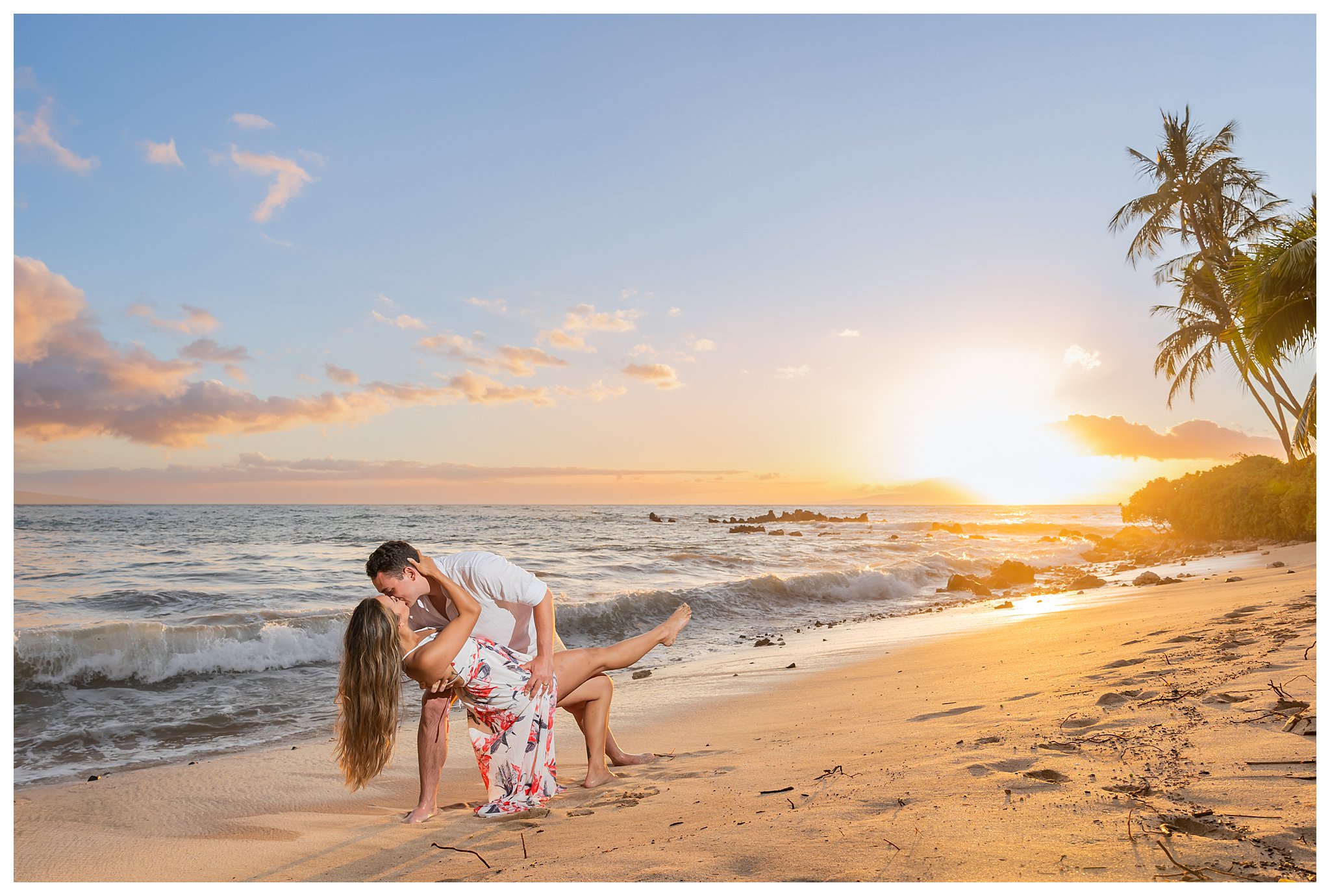Two people pose on the beach in front of the ocean during sunset