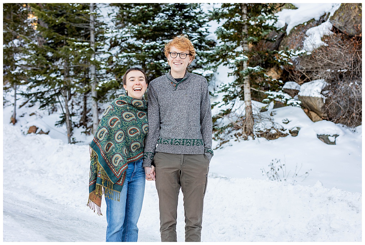 A couple poses in front of snow and rocks.