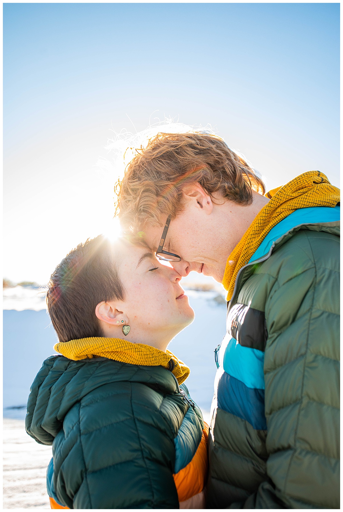 An up close photo of a couple with their foreheads pressed together, snow in the background.