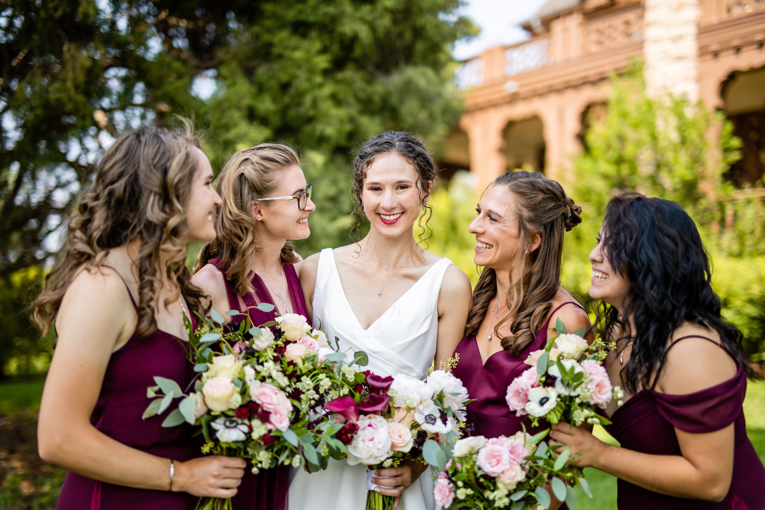 A bride poses with her bridesmaids in dark maroon dresses.