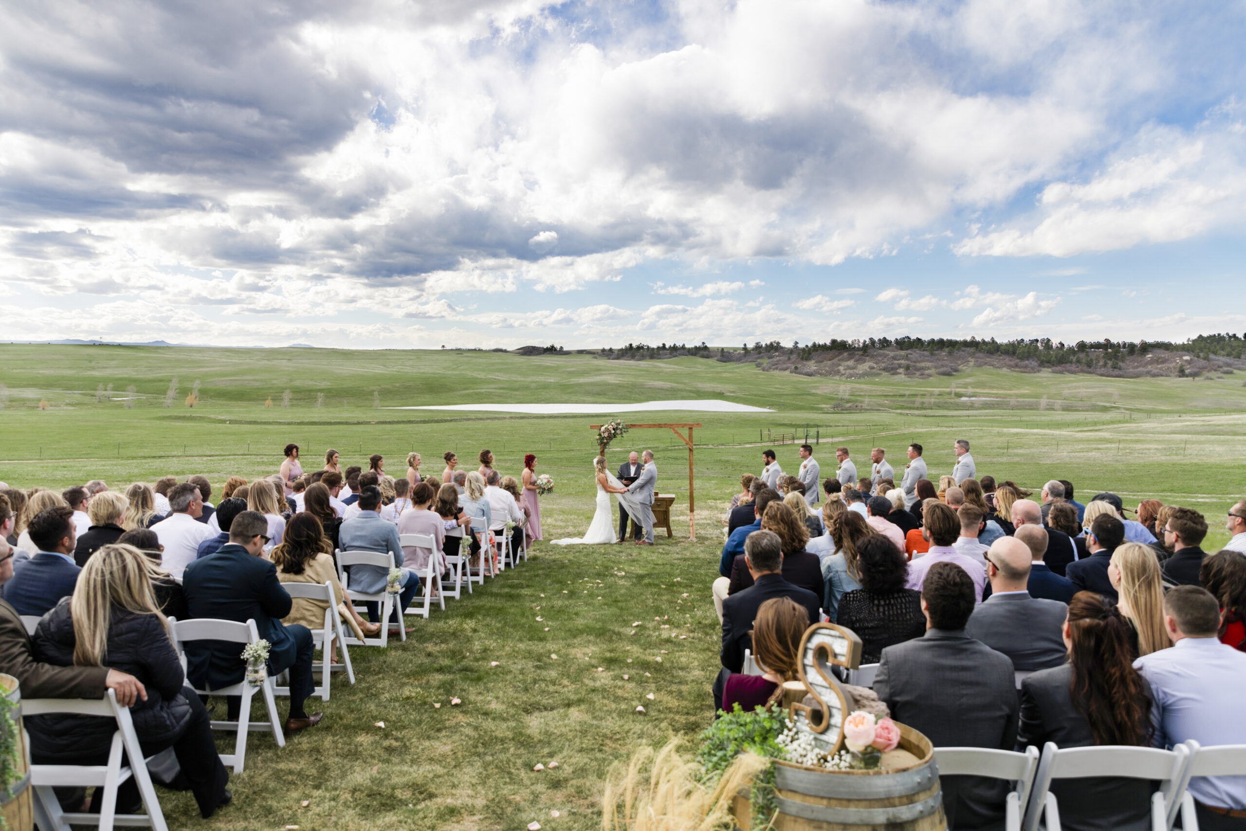 A couple gets married on a green field with a dramatic sky behind them.