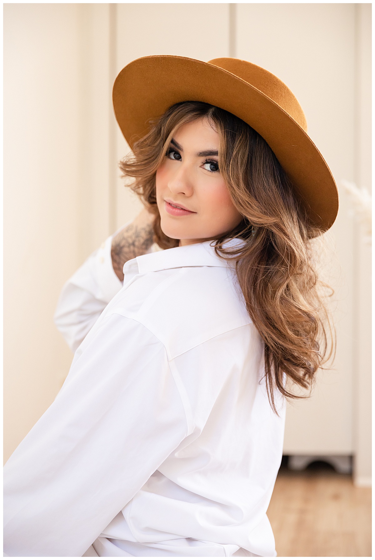 A woman poses in a white button-down shirt and a brown felt hat in a boudoir session