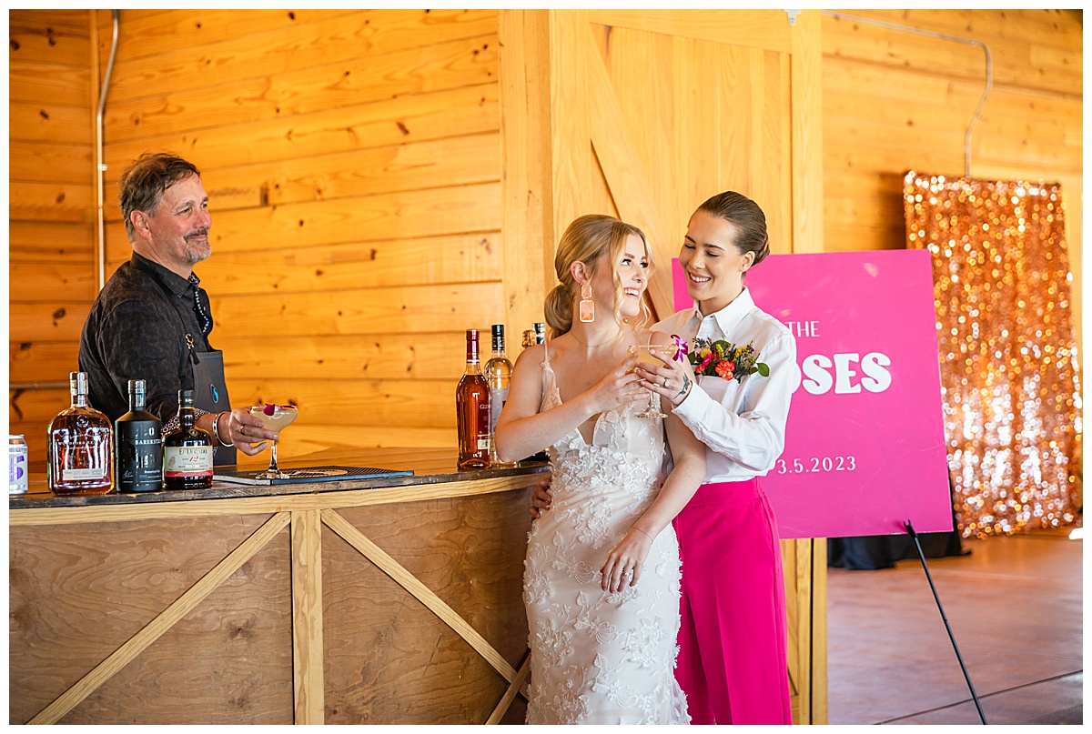 The two brides get a cocktail from the bartender at this pink wedding inspiration photo shoot.