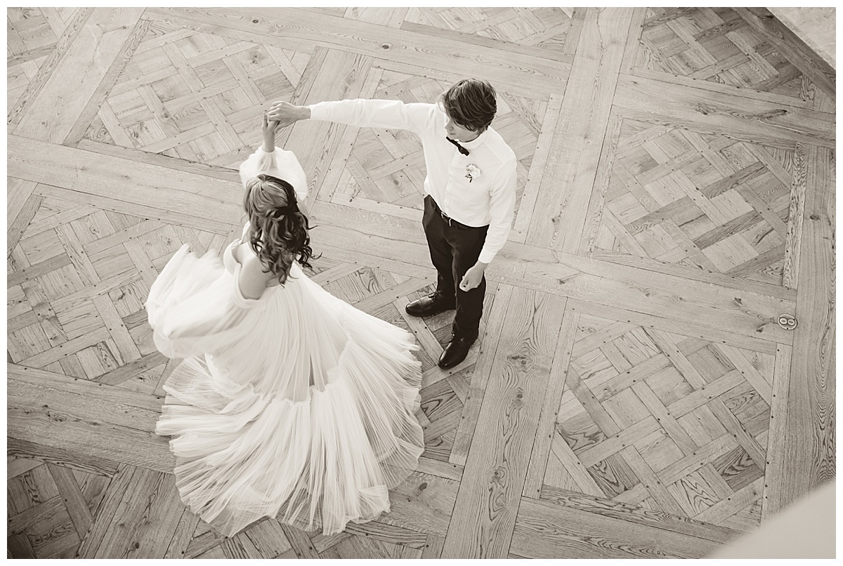 A man and woman dance on the dance floor. He spins her and her dress twirls around. This image is in black and white.