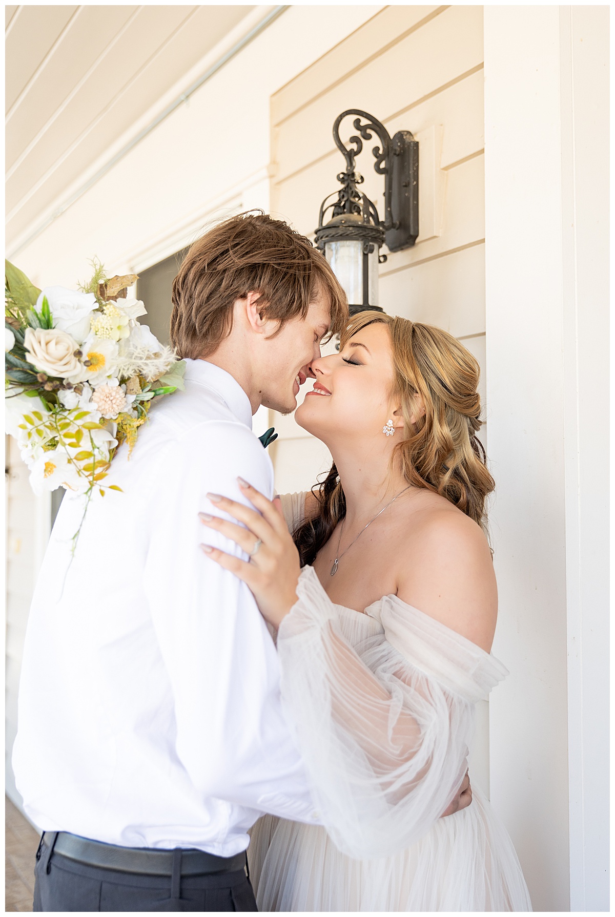 A bride and groom kiss and smile at each other outside on the porch of the mansion.