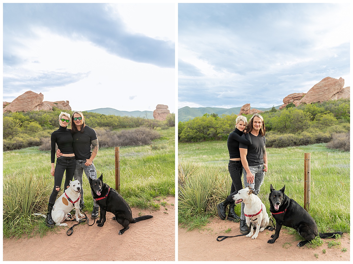 A couple dressed in black pose in front of a field of grass and large red rocks with their dogs for their dog couples session