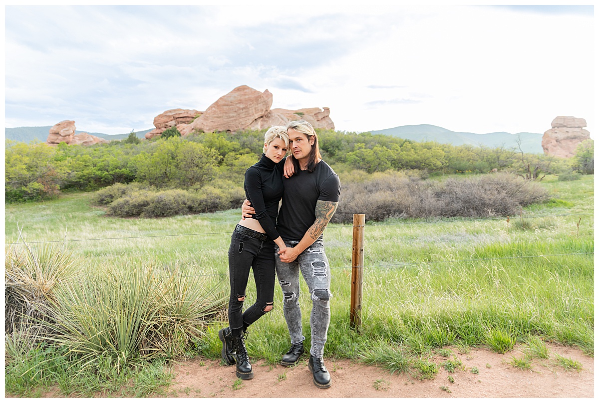 A couple dressed in black pose in front of a field of grass and large red rocks