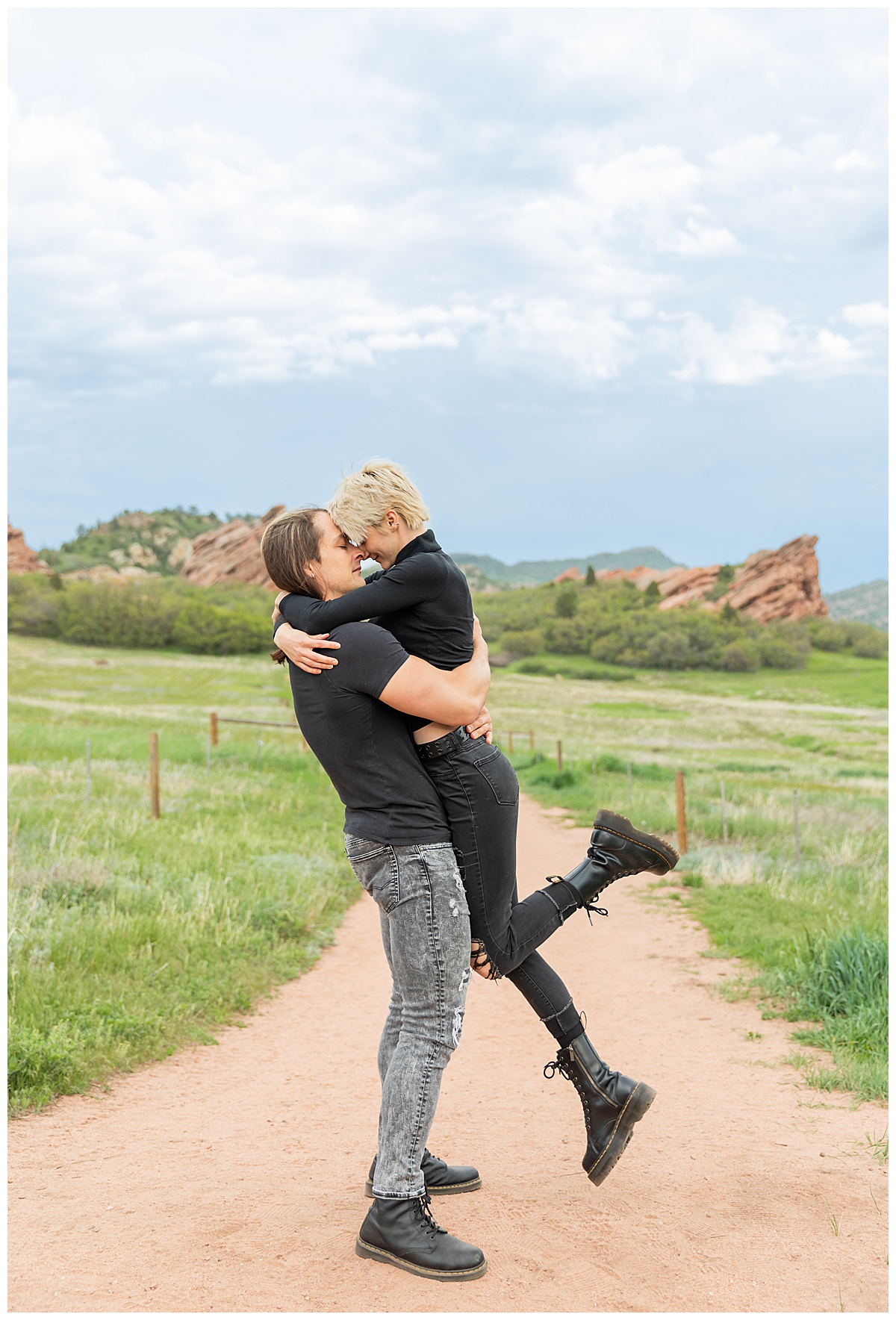 A couple dressed in black pose in front of a field of grass and large red rocks