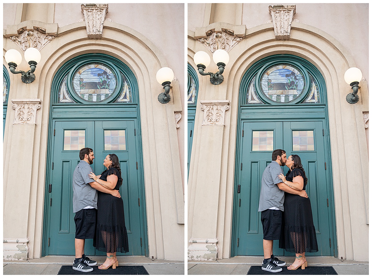 A couple in black and gray pose in front of an old pink and green church with a teal door