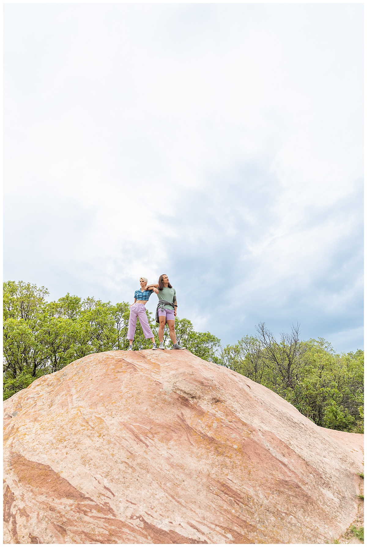 A couple dressed in purple, blue, and green pose on top of a large red rock