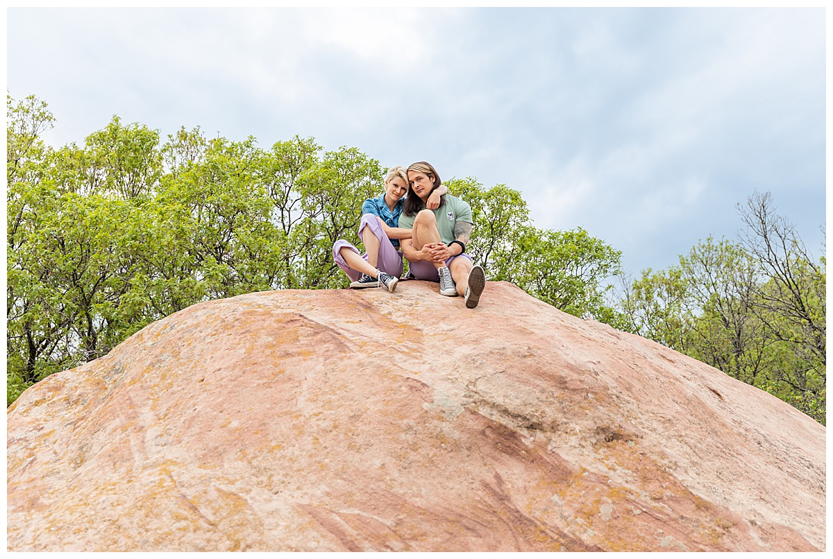 A couple dressed in purple, blue, and green pose on top of a large red rock