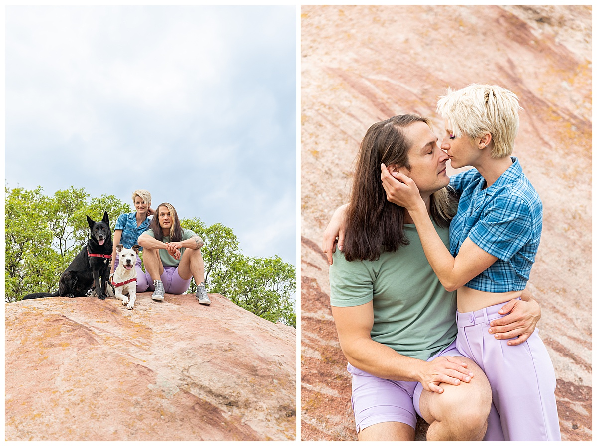 A couple dressed in purple, blue, and green pose on top of a large red rock with their dogs at their dog couples session