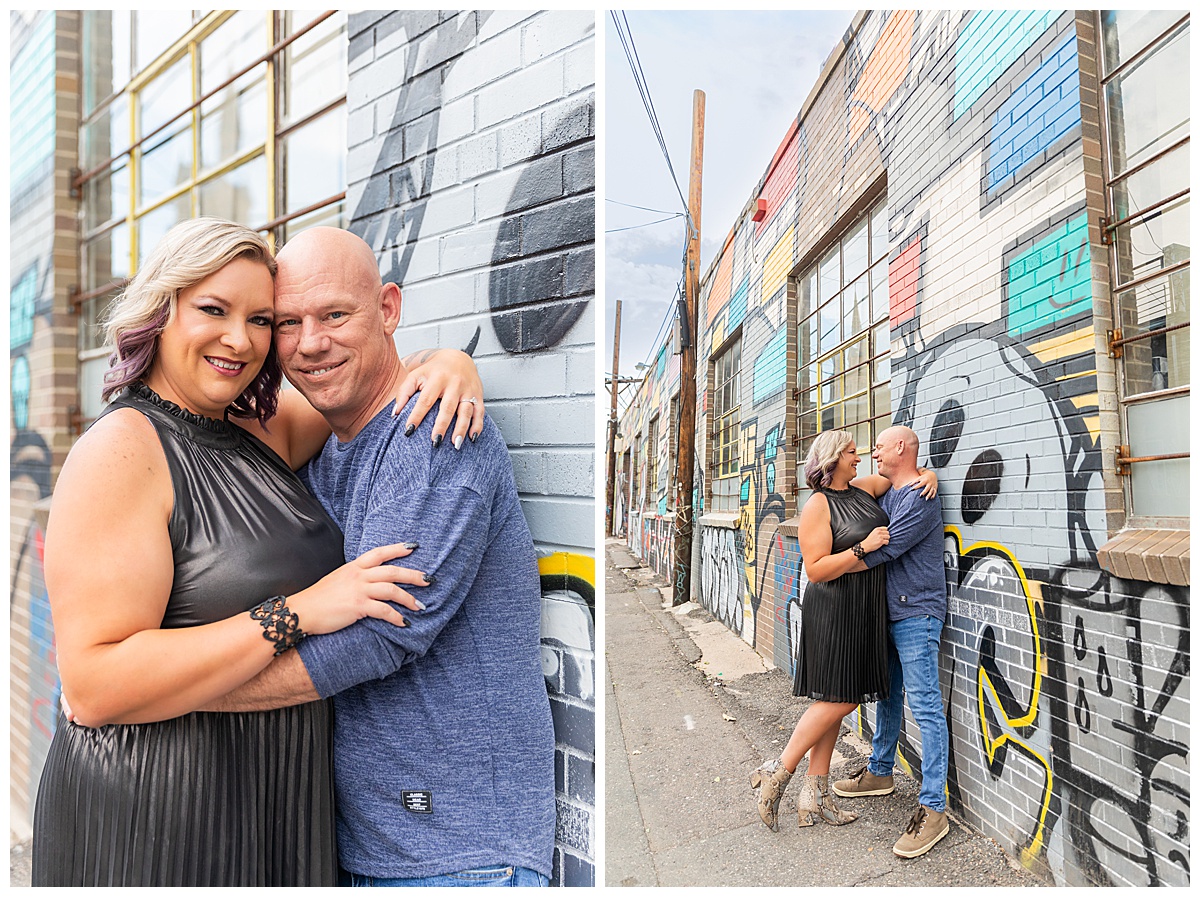 A woman with blonde hair dark silver dress and a bald man in a blue sweater pose in front of a mural in downtown Denver, Colorado