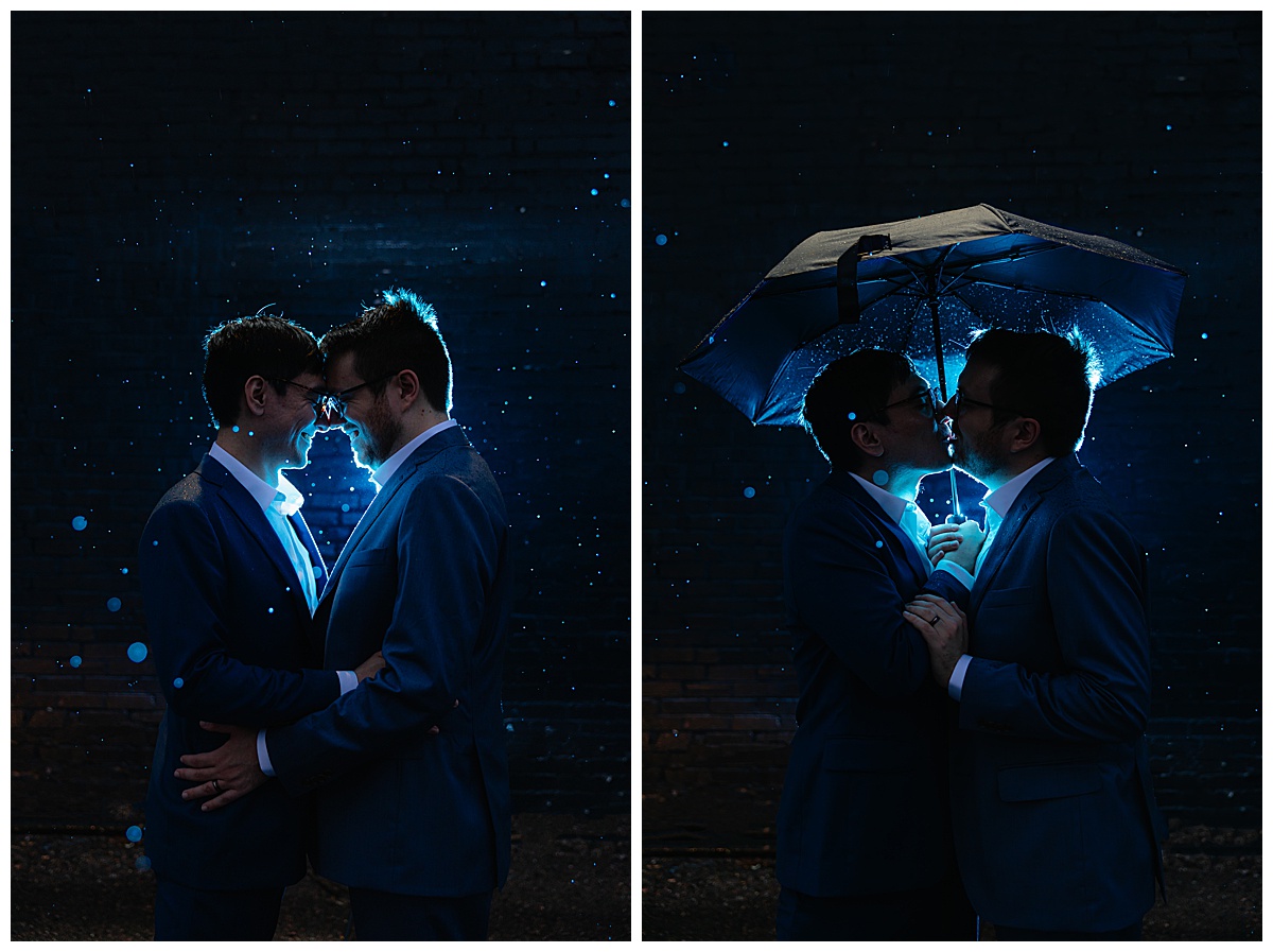 Two men pose in the dark with a bright blue light behind them. Rain is coming down around them