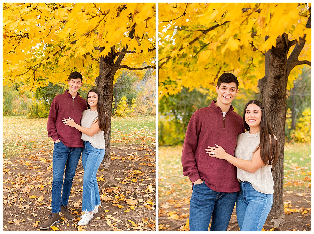 A couple poses in front of a bright yellow tree. The man is wearing a red sweater and blue jeans, the woman is wearing a sleeveless cream sweater and blue jeans.