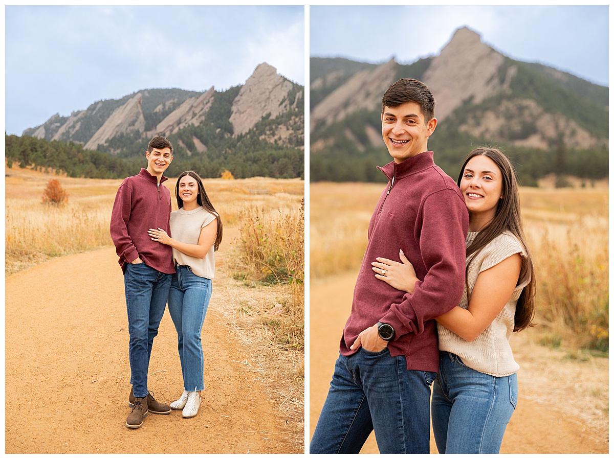 A couple poses in front of the Boulder flatirons. The man is wearing a red sweater and blue jeans, the woman is wearing a sleeveless cream sweater and blue jeans.