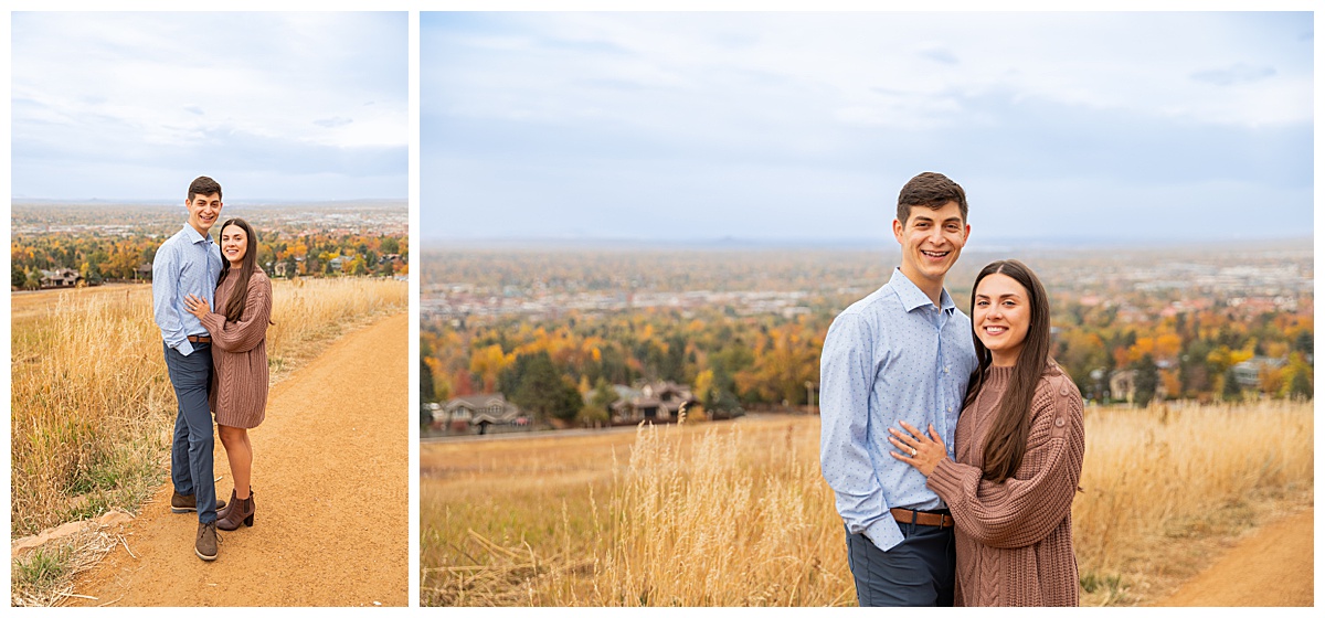 A couple poses overlooking Boulder, CO. The man is wearing a blue button down and navy dress pants, the woman is wearing a mauve sweater dress.