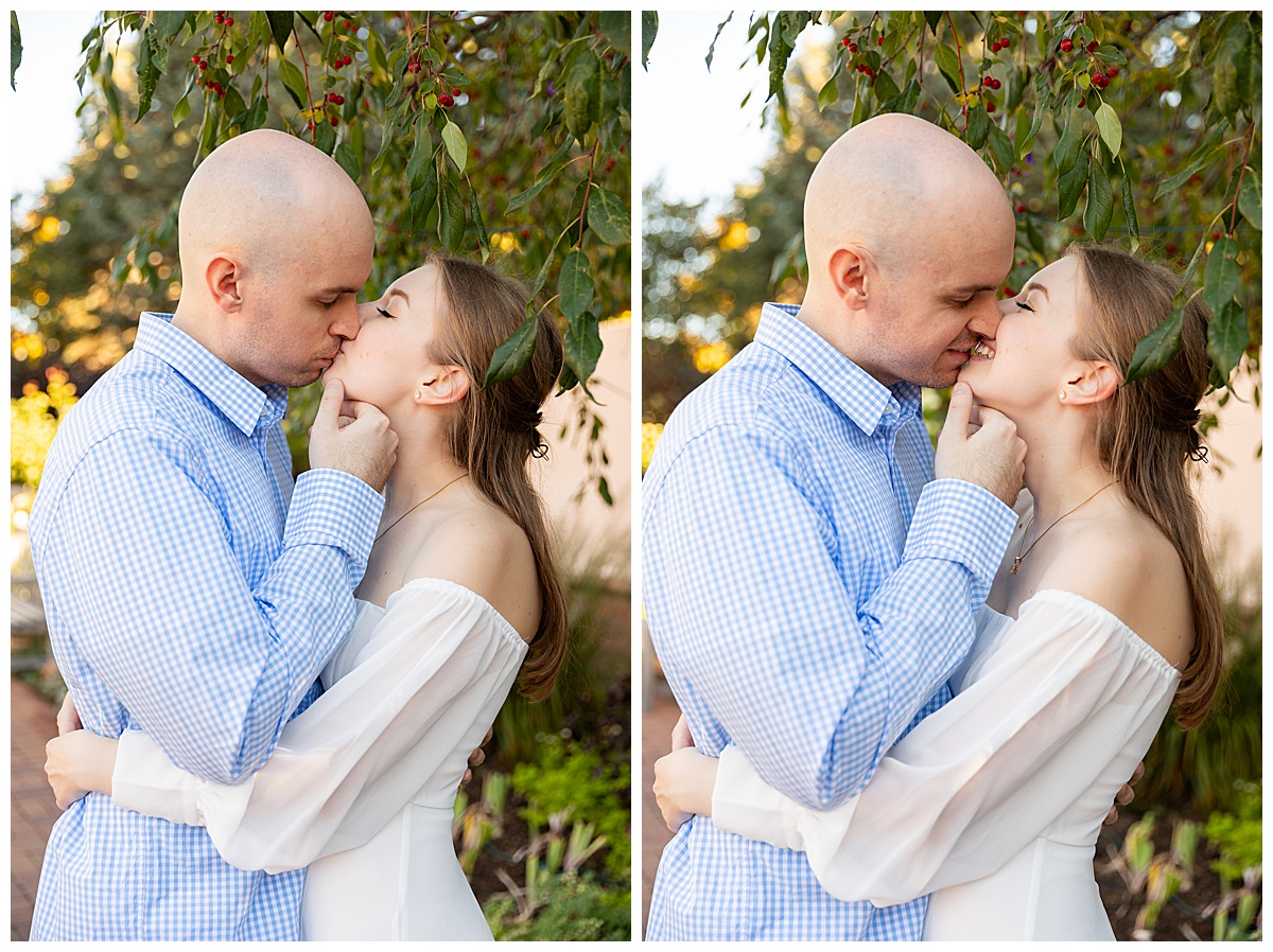 A couple poses for their botanic gardens engagement session. The blonde woman is wearing a white long sleeve dress and the bald man is wearing a blue plaid shirt and jeans.