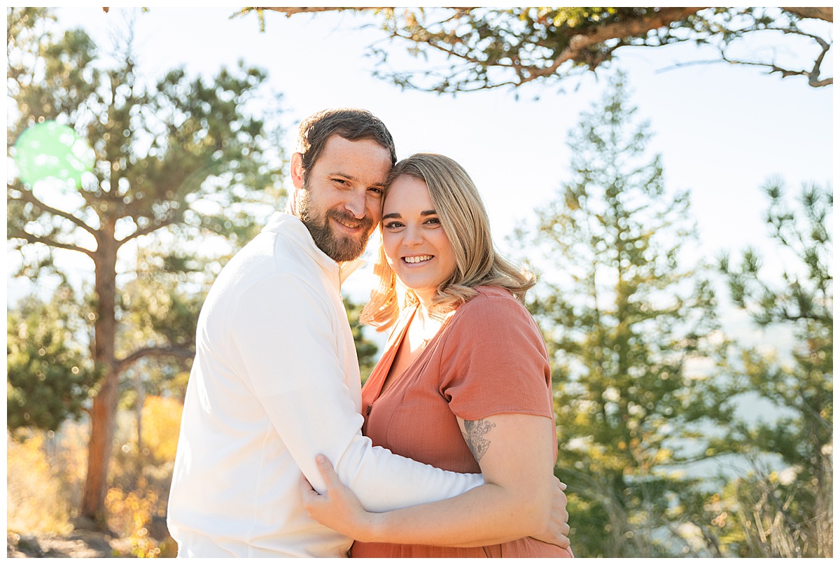 A couple poses for their Lookout Mountain couples session. The woman is wearing a terracotta linen dress and the man is wearing a white jacket and blue jeans. 