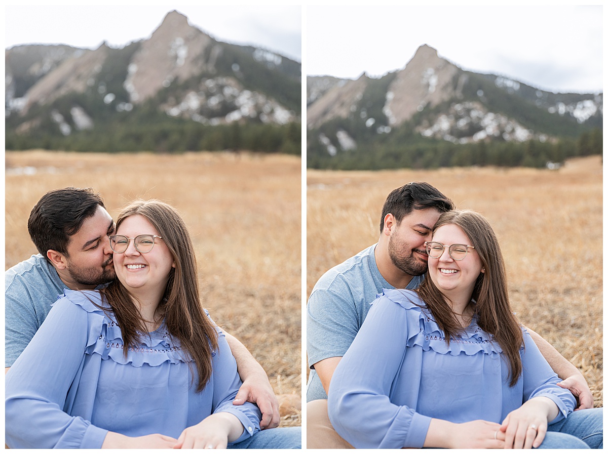 A couple poses in front of the Flatirons for their Boulder engagement session.  They are both wearing blue; the man has dark brown hair and a beard, the woman has long brown hair and glasses.