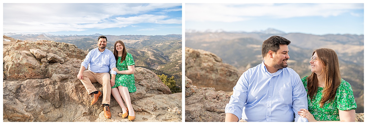 A couple poses on rocks in front of the Colorado Rocky Mountain range. The man is wearing a blue button-down shirt and tan pants. The woman is wearing a green dress with flowers.