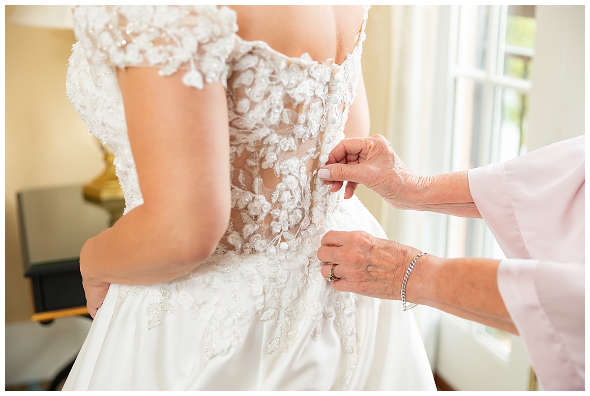 A bride puts her lace ballgown wedding dress on with her mother's help