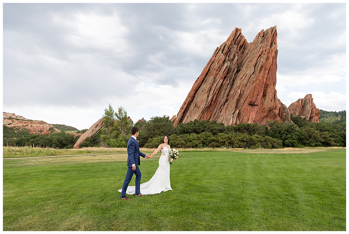 The couple pose on the golf course for bridal portraits. She is holding her bouquet. There are big red rocks in the background.