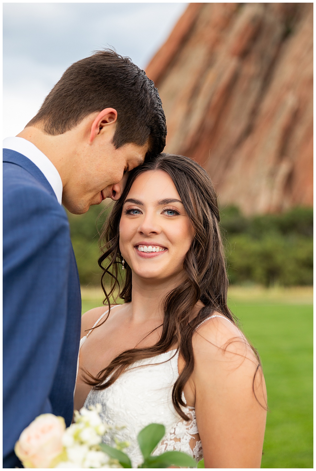 The couple pose on the golf course for bridal portraits. She is holding her bouquet. There are big red rocks in the background.