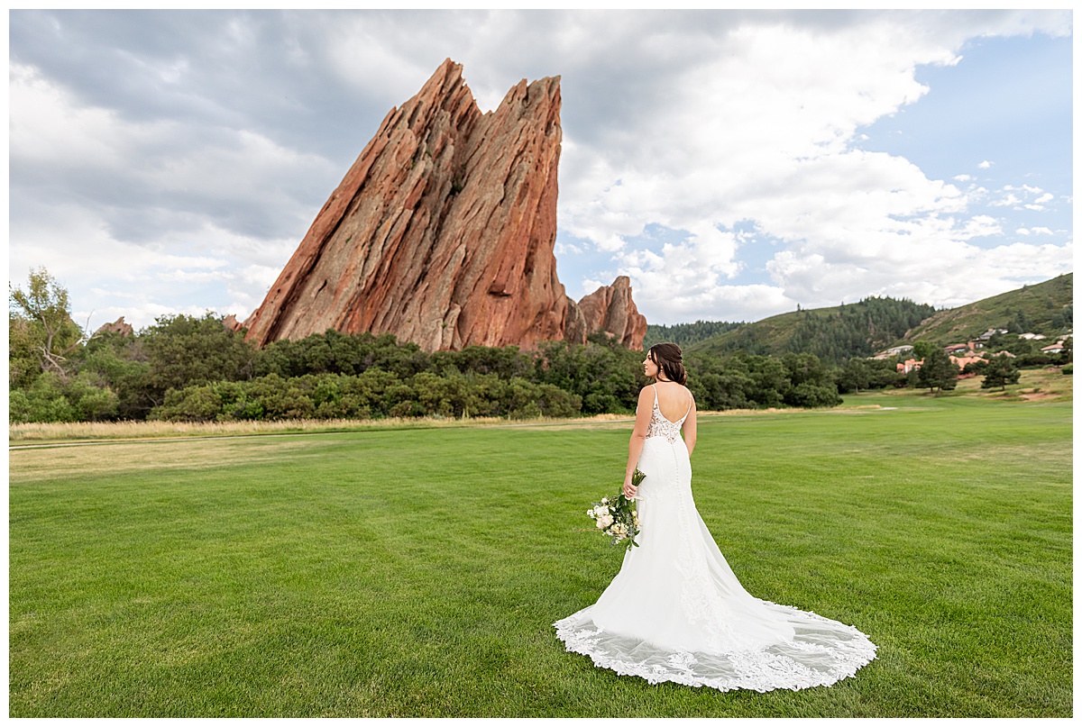 The couple pose on the golf course for bridal portraits. She is holding her bouquet. There are big red rocks in the background.