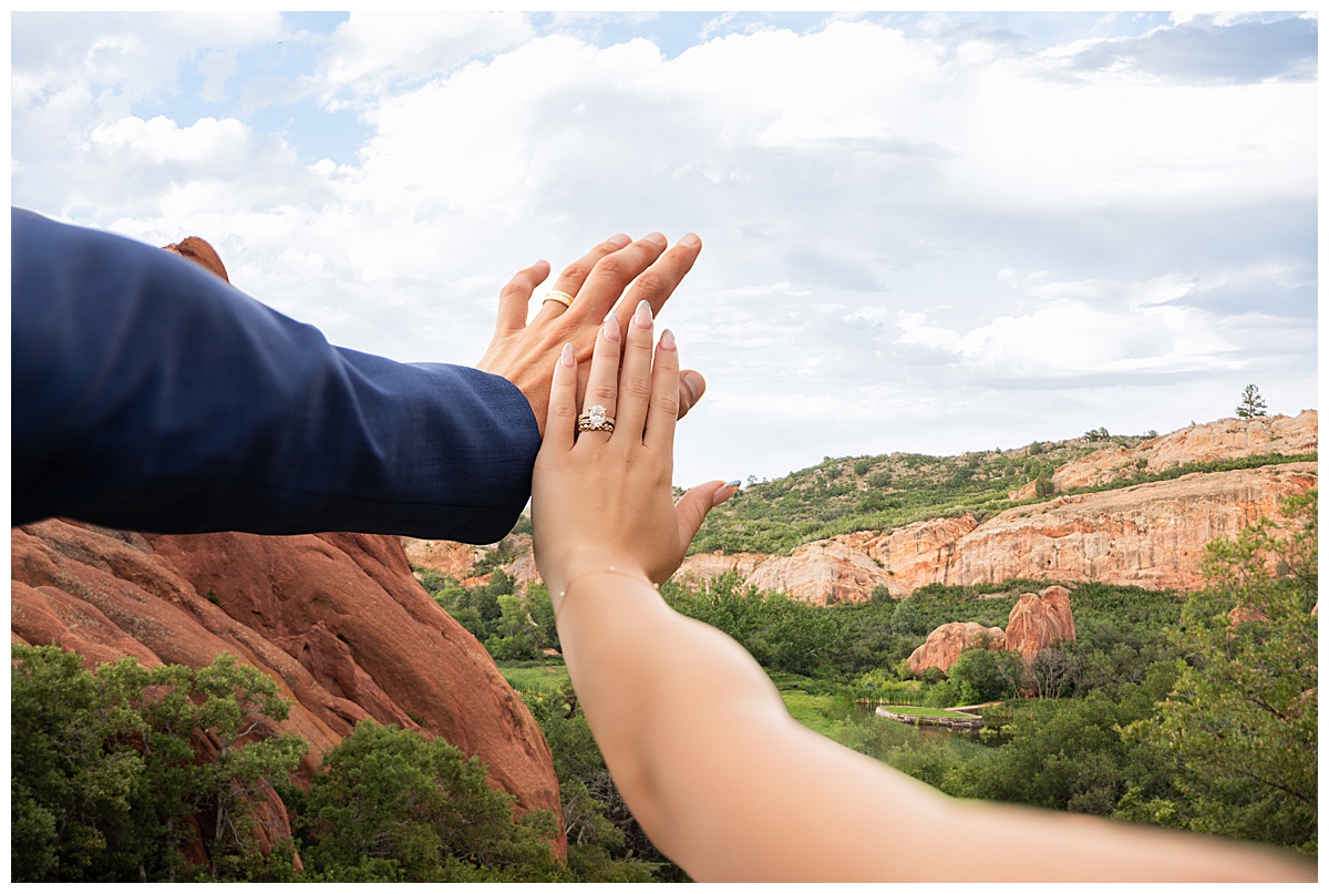 The couple pose on the golf course for bridal portraits. She is holding her bouquet. There are big red rocks in the background.