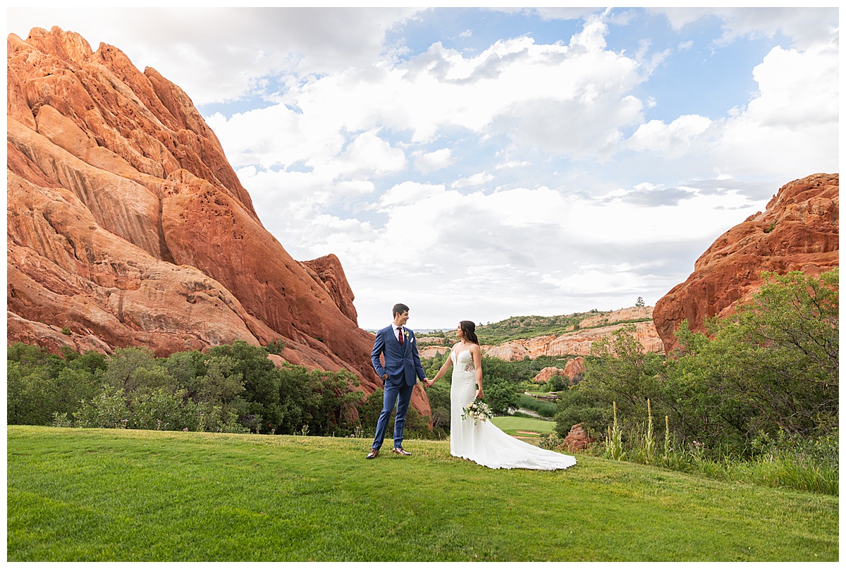 The couple pose on the golf course for bridal portraits. She is holding her bouquet. There are big red rocks in the background.