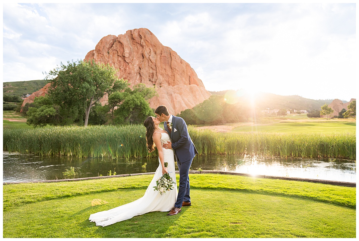 The couple pose on the golf course for bridal portraits. She is holding her bouquet. There are big red rocks in the background.