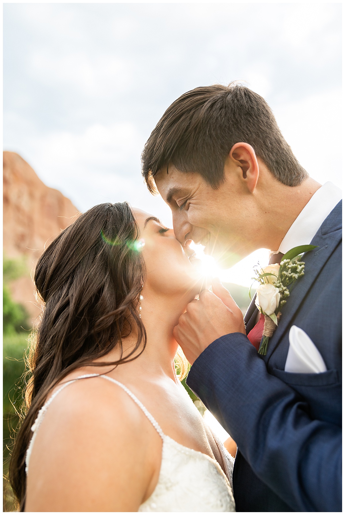 The couple pose on the golf course for bridal portraits. She is holding her bouquet. There are big red rocks in the background.