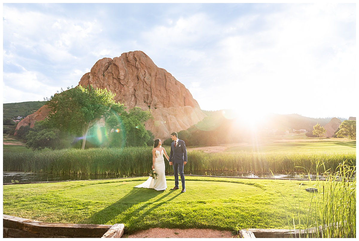 The couple pose on the golf course for bridal portraits. She is holding her bouquet. There are big red rocks in the background.