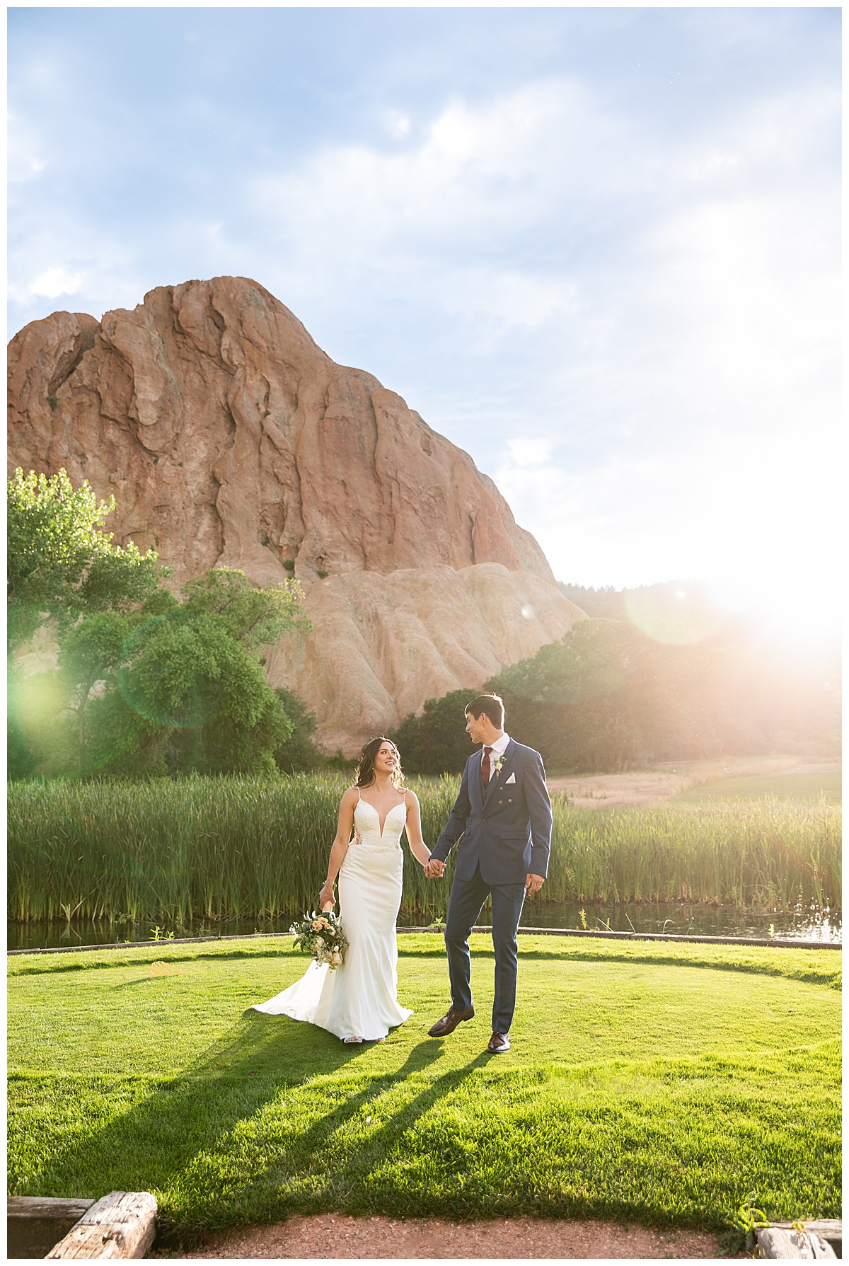 The couple pose on the golf course for bridal portraits. She is holding her bouquet. There are big red rocks in the background.