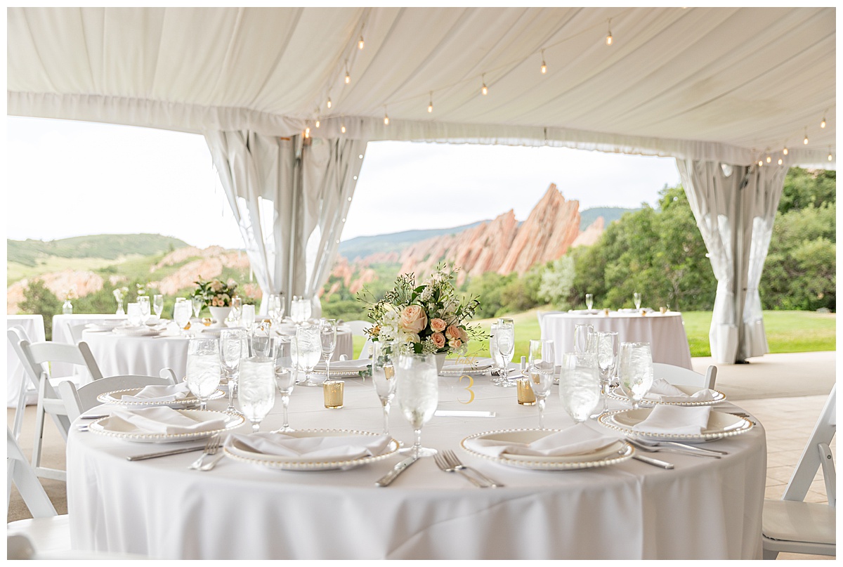 A photo of the reception tent before the guests come in to sit down. Everything is white with gold accents and pink and green flowers on the tables.