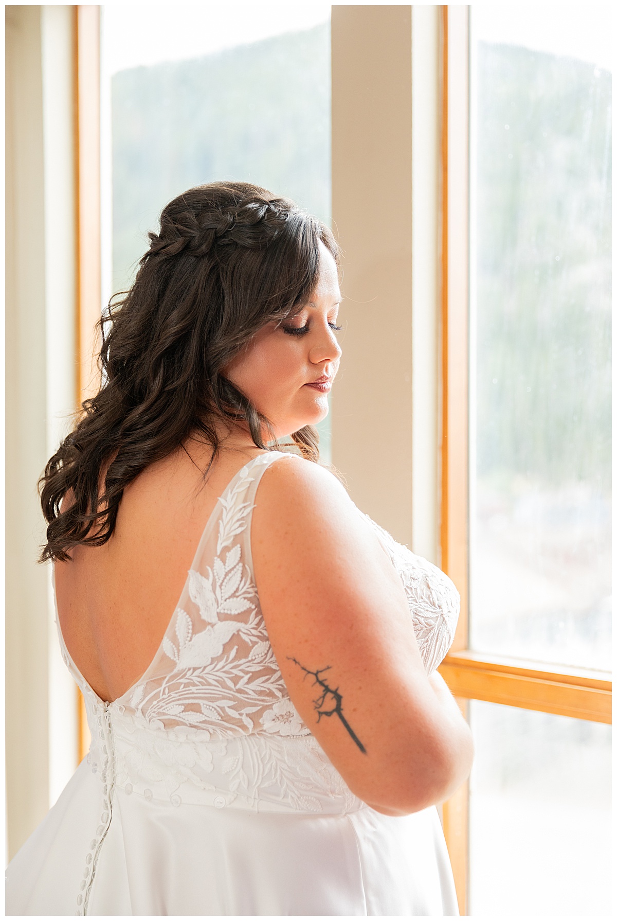 The bride's poses in front of the window after getting dressed. She has long dark brown hair in a half updo.