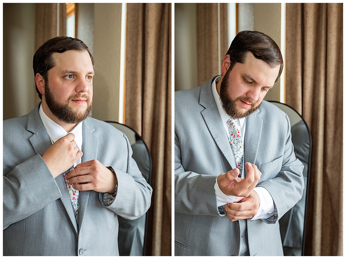 The groom gets ready by fixing his tie and cufflinks. He is wearing a gray suit and floral tie.