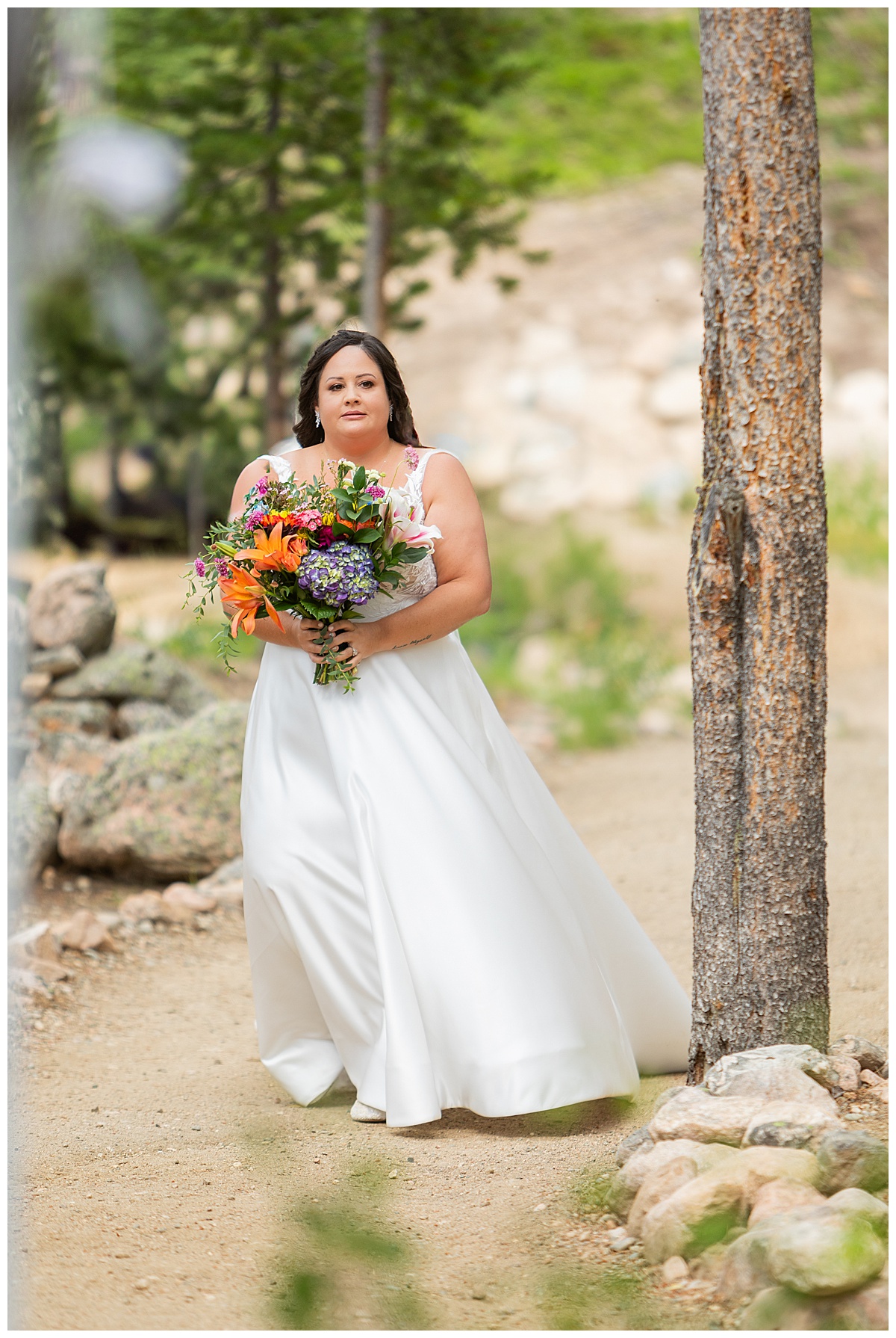 The bride walks herself down the aisle. She is wearing a white a-line wedding dress and carrying a bouquet of brightly colored wildflowers.