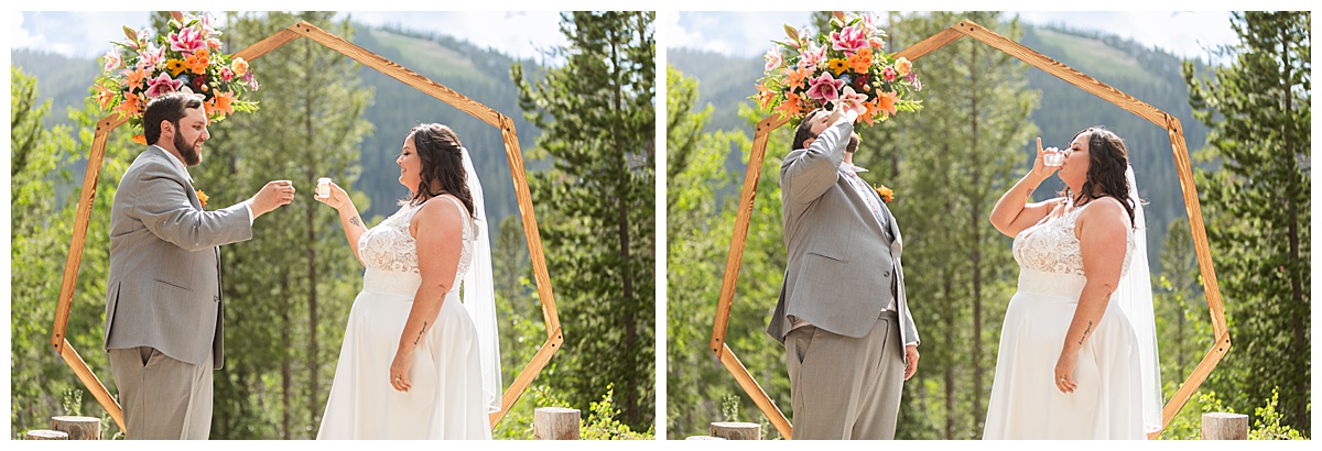 The bride and groom get married at Winter Park Mountain Lodge. They are taking a shot of limoncello in honor of the groom's father. A heptagonal arch, pine trees, and a mountain are behind them.