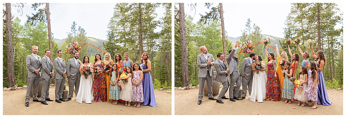 The bride, groom, and bridal party are posing for photos. The men are wearing gray suits and the women are in different colored dresses. Pine trees and a mountain are behind them.