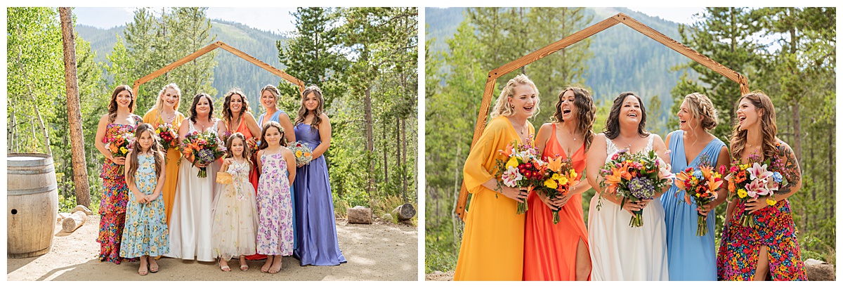 The bride and bridesmaids are posing for photos. The bridesmaids are all wearing different colored dresses. Pine trees and a mountain are behind them.