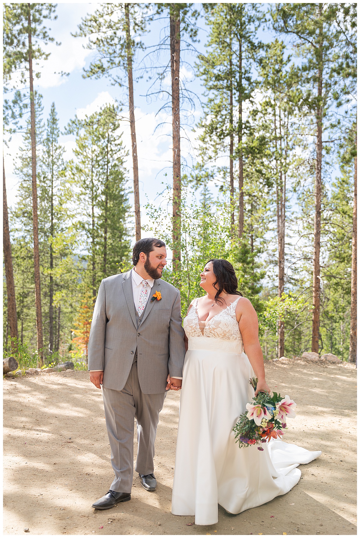 The bride and groom pose for photos. Pine trees are behind them.