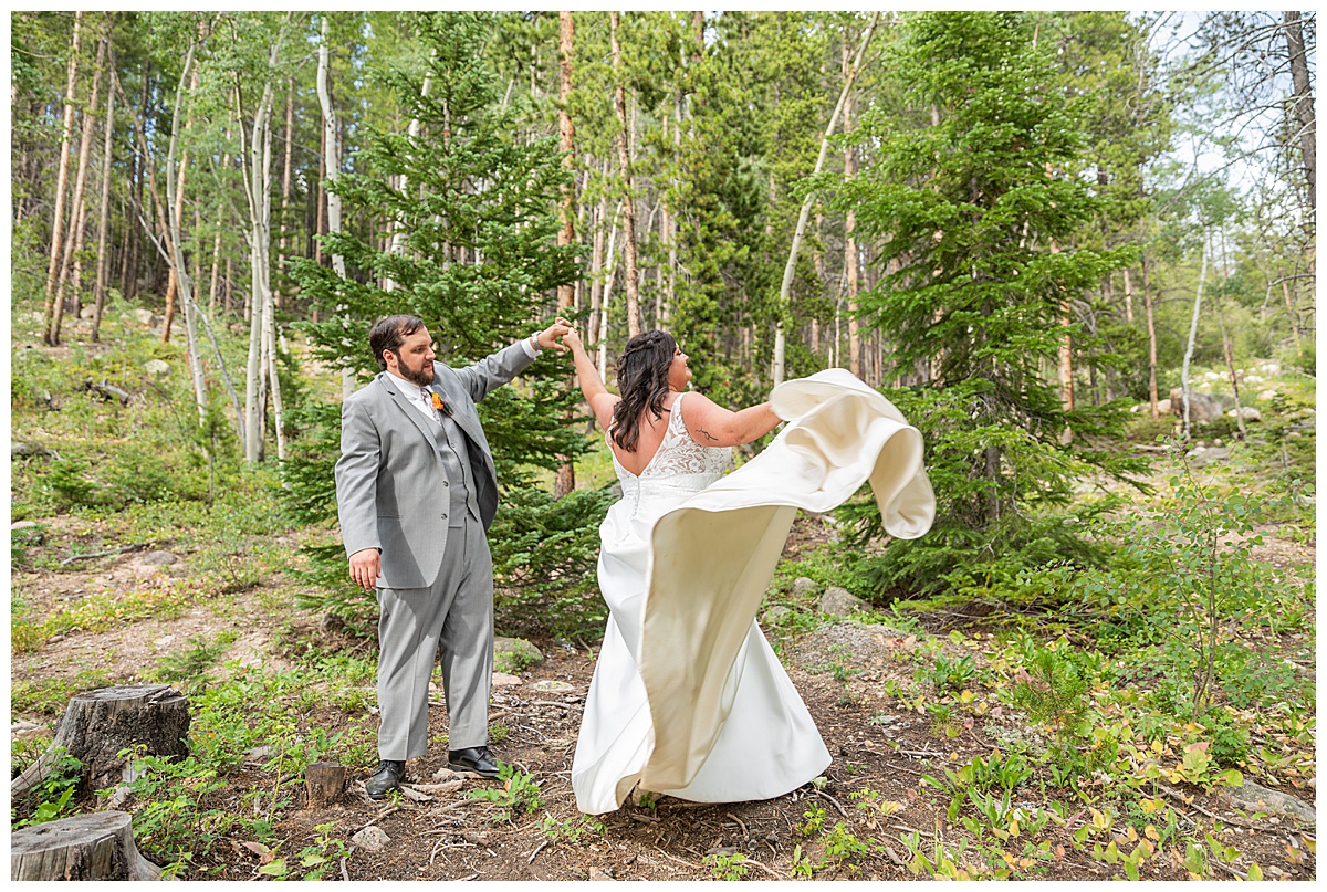 The bride and groom pose for photos. They are dancing in a grove of pine trees.