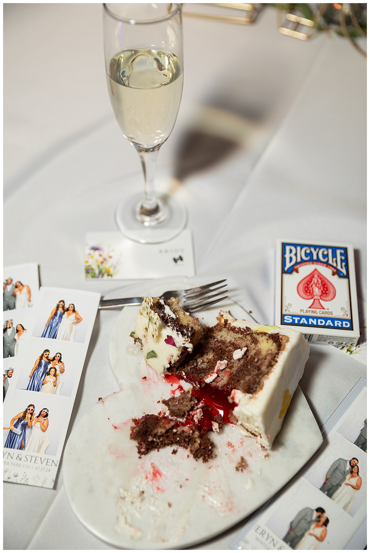 A close up of half-eaten cake on the couple's sweetheart table. There is also a glass of champagne, a deck of cards, a heart platter that the cake is sitting on, and photo strips from the photo booth.