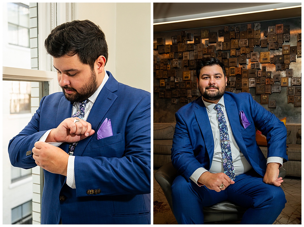 The groom gets ready in the hotel lobby. He has dark brown hair and a beard. He is wearing a blue suit with a floral tie.