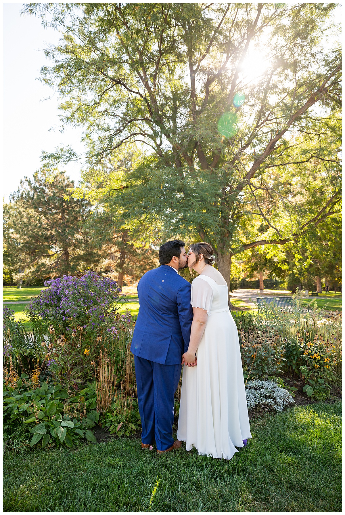 The bride and groom kiss and pose next to a garden of purple and yellow flowers.