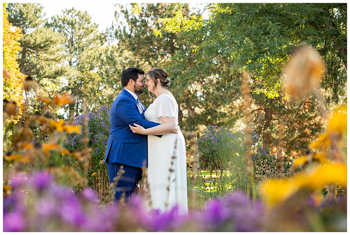 The bride and groom kiss and pose next to a garden of purple and yellow flowers.