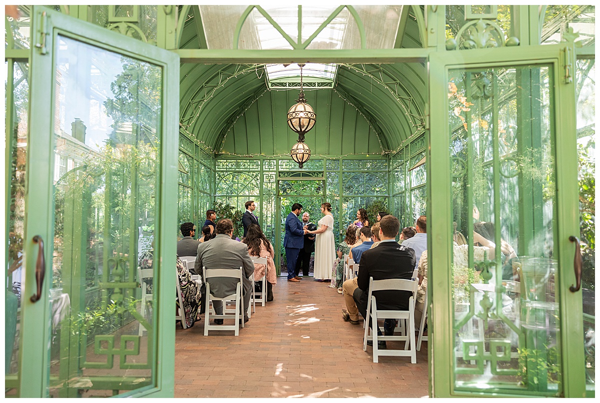 The bride and groom have their ceremony in the green metal Woodland Mosaic Solarium at their Denver Botanic Gardens wedding.