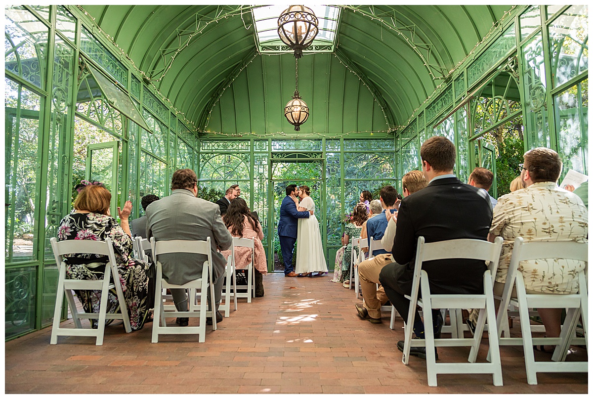 The bride and groom have their ceremony in the green metal Woodland Mosaic Solarium at their Denver Botanic Gardens wedding.